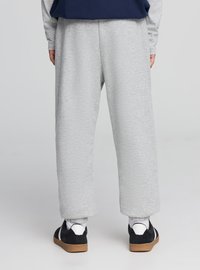 Jasnoszare spodnie dresowe o luźnym kroju, zwężane nogawki i elastyczna talia. Połączone z czarnymi trampkami z białymi akcentami.