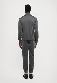 Chándal gris oscuro hecho de tejido suave, con cuello con cremallera, puños y cinturilla acanalados, combinado con calzado negro.