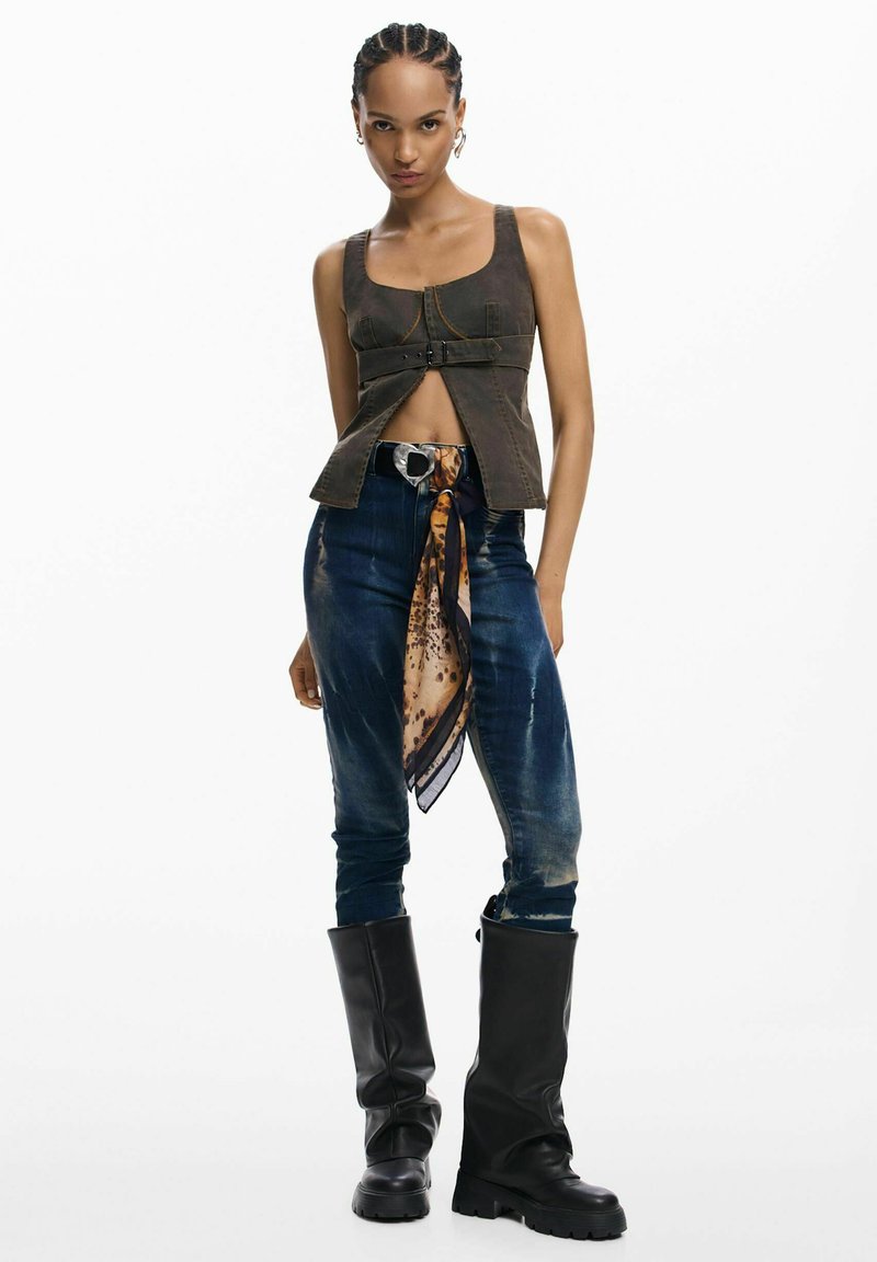 Pruun lühike topp vööga, kulunud sinised teksad, mille külge on talje ümber seotud mustriga sall, ja põlvekõrgused mustad saapad.