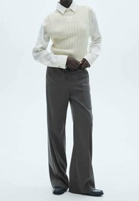 Un gilet en tricot crème clair sur une chemise blanche à boutons ; un pantalon large gris avec une ceinture à cordon ; des chaussures plates noires. Design minimaliste.