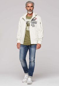 White jacket with a hood and zipper details, green graphic t-shirt, blue jeans, and white sneakers. Simple design with printed accents.