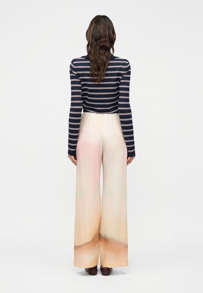 Γυναίκα με μακριά κυματιστά μαλλιά φοράει μπλε σκούρο ριγέ μακρυμάνικη μπλούζα που είναι φουσκωμένη μέσα σε ψηλόμεσο, φαρδύ, ομπρέ παντελόνι και καφέ παπούτσια.