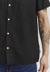 Sorte kortærmede knap-op skjorte lavet af struktureret stof, med hvide knapper og en brystlomme, parret med blå denim jeans.