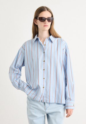 Light blue button-up shirt with vertical red stripes, long sleeves, and a collar. Features gold buttons and relaxed fit. Worn with dark sunglasses.