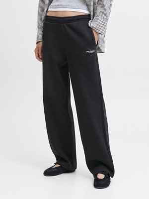 Black, loose-fit sweatpants with an elastic waistband and side pockets. Notable branding "J.JAX STUDIO" in white detailing. Soft fabric.