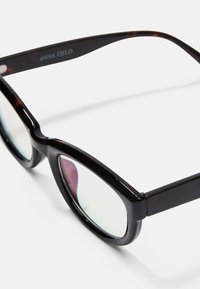 Sunglasses ar bruņurupuča krāsas rakstu, tumšiem plastmasas ietvariem, modernā formā, skaidriem stikliem un logotipu uz templja.