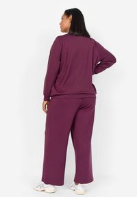 Conjunto de ropa de estar en púrpura que incluye una camiseta de manga larga de corte holgado y pantalones de pierna ancha. Tejido suave con una textura lisa. Zapatillas blancas.