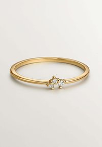 Anillo de oro con una banda delgada que presenta tres pequeñas gemas transparentes en un engaste de racimo. Textura suave con un acabado pulido.