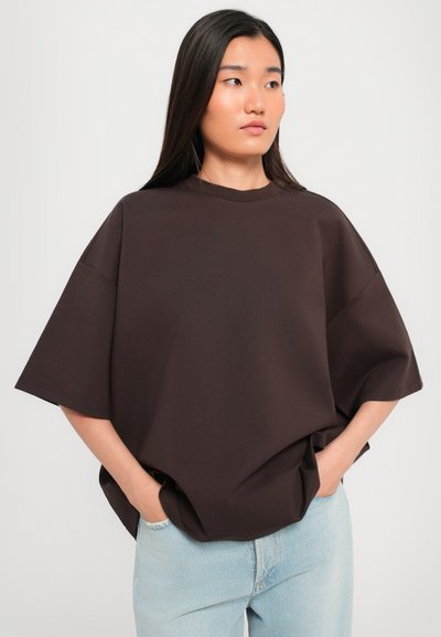 T-shirt marrone oversize con collo rotondo e spalle scese, realizzata in tessuto morbido, abbinata a jeans in denim blu chiaro.
