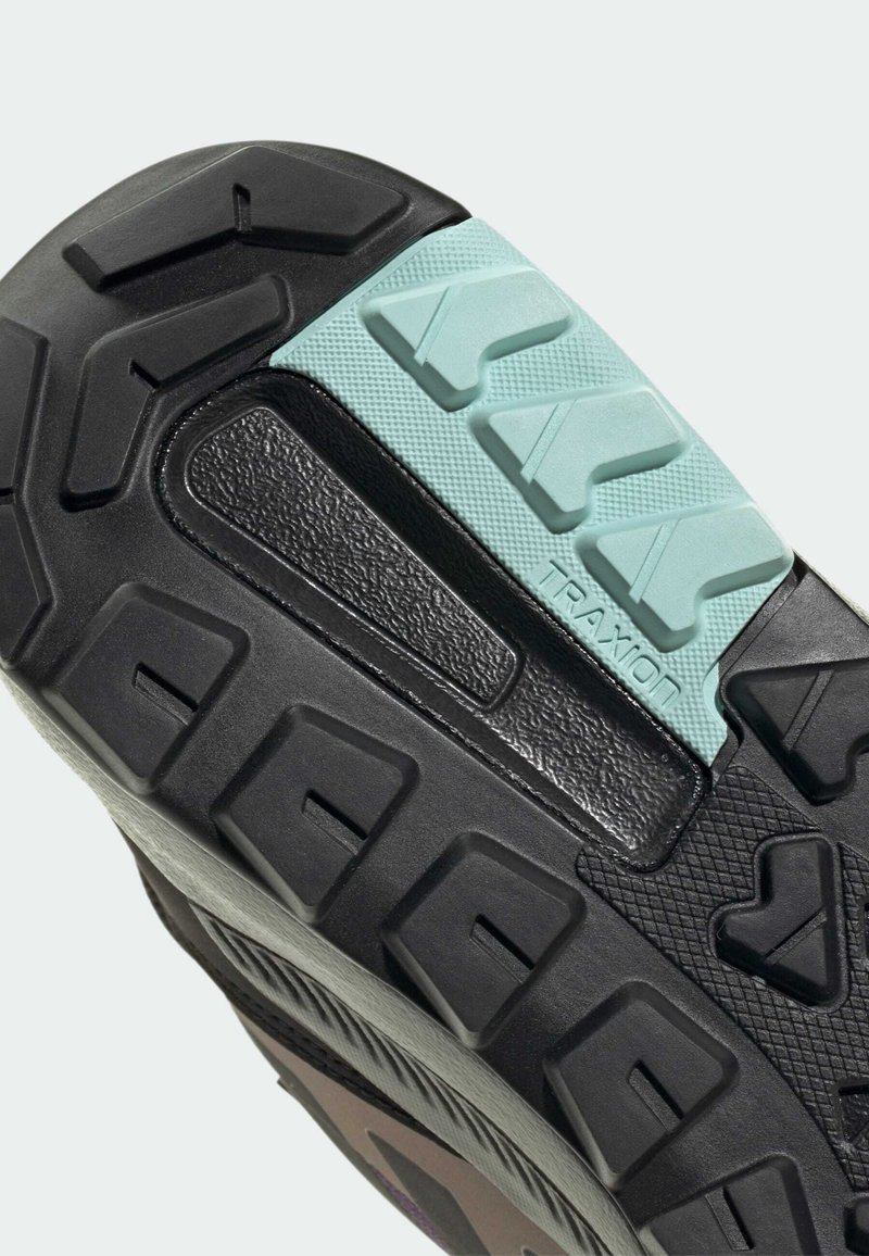 Suela de zapato negra con patrones texturizados y una sección de acento azul claro. Presenta ranuras profundas para tracción y material de goma para durabilidad.