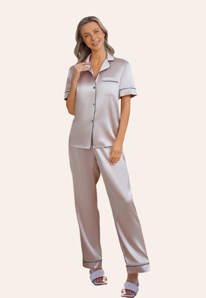 Ensemble de pyjama en satin de couleur beige clair avec des passepoils noirs. La chemise à manches courtes à boutons possède une poche sur la poitrine. Le pantalon est ample avec une taille élastique.