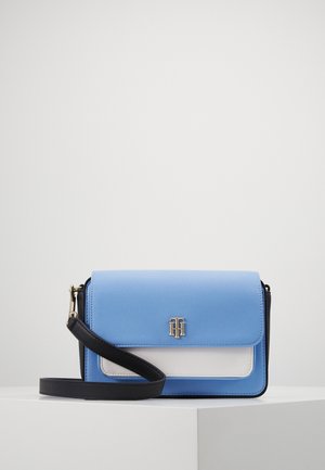 Blå og hvid rektangulær crossbody taske med sort rem og guldfarvet logo på frontklappen, vist på en hvid overflade.