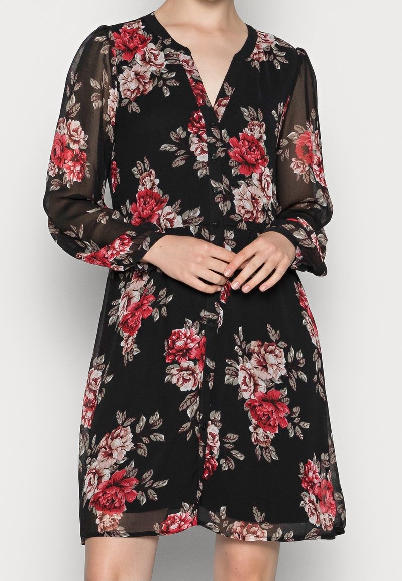 Schwarzes Blumenkleid mit langen, transparenten Ärmeln, V-Ausschnitt und Knopfdetail. Mit roten und pinken Rosen auf dunklem Hintergrund.