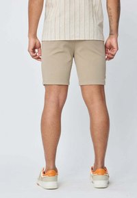 Shorts beiges arrivant au genou en tissu lisse, associés à des baskets blanches avec des accents orange. Texture côtelée visible sur le t-shirt.