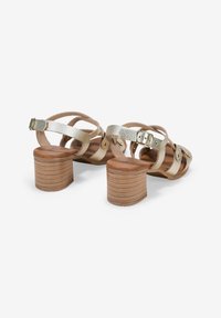 Sandalias de tacón con tiras, con cruces de metal dorado y plateado, parte superior texturizada y un tacón de bloque de madera apilada.