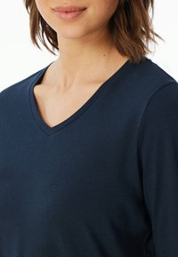 Top blu navy a V realizzato in tessuto morbido, caratterizzato da una vestibilità slim e una texture liscia, con maniche corte e dettagli di design minimi.