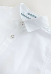 Wit overhemd met kraag en twee zichtbare witte knopen met het merk "Ted Baker" op een schone, lichte achtergrond.