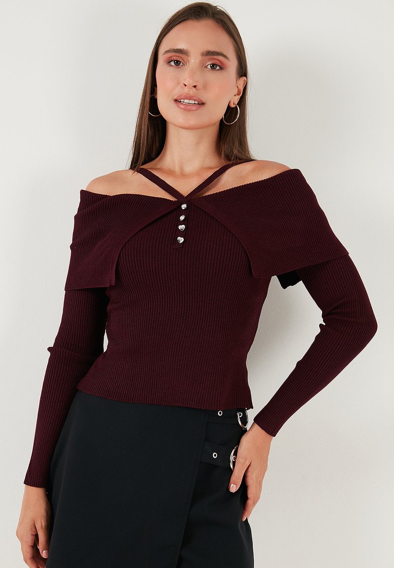 Woman wearing a ribbed, off-shoulder burgundy sweater with silver heart-shaped buttons and a black skirt with buckle details.