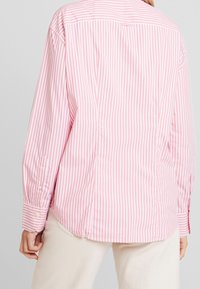 Růžovo-bílé proužkované tričko s dlouhým rukávem, s knoflíkovou légou vpředu, límečkem a manžetami na rukávech, s volným střihem a hladkou texturou.
