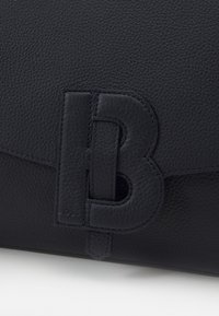 Ciemnoniebieska skórzana torebka o ziarnistej fakturze. Posiada duże wytłoczone logo oraz zapięcie na klapkę. Szwów widocznych wzdłuż krawędzi.