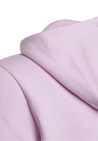 Close-up van een lichtpaarse hoodie die de naad en de ingevouwen capuchon toont op een effen witte achtergrond.