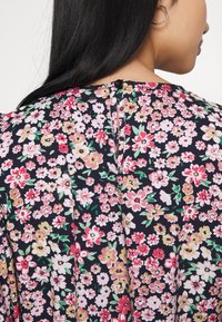 Blusa floral con un fondo azul marino oscuro, que presenta una mezcla de pequeñas flores coloridas en rosa, rojo y amarillo. Cierre de botones en el cuello.