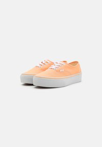 Zapatillas de lona naranjas con un diseño de caña baja, cordones blancos y una suela de goma blanca gruesa sin patrones ni acentos visibles.