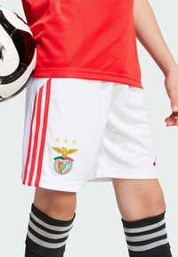 Pantalones cortos de fútbol blancos con acentos rojos, que presentan el logotipo del equipo Benfica y tres estrellas. Calcetines a rayas en blanco y negro completan el atuendo.