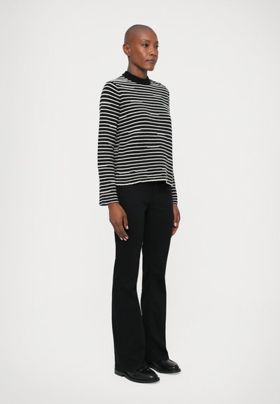 Maglione a righe bianche e nere con scollatura rotonda e maniche lunghe, abbinato a pantaloni neri a zampa d'elefante e scarpe nere.