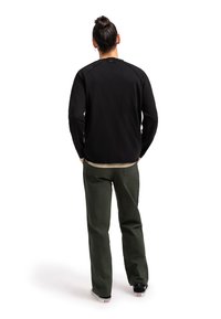 Felpa nera con collo a giro e cuciture rinforzate sulle spalle, abbinata a pantaloni verdi. Stilizzata con scarpe nere e una maglietta beige sotto.