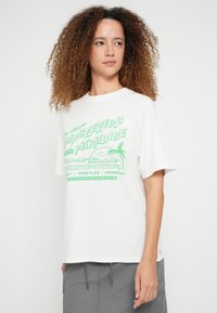 Λευκό βαμβακερό t-shirt με κοντά μανίκια και στρογγυλή λαιμόκοψη. Διαθέτει πράσινο γραφικό κείμενο και σχέδιο με φοίνικα στην πρόσοψη.