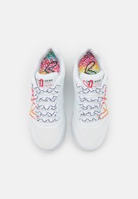 Weiße Sportschuhe mit durchlochten Details, bunten, gemusterten Innensohlen und schwarz-weißen Schnürsenkeln mit einem linearen Design.