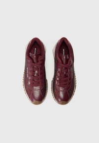 Para burgundowych skórzanych i materiałowych sneakersów z sznurówkami oraz teksturowanymi gumowymi podeszwami, pokazana z góry na białym tle.