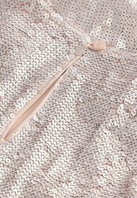 Tissu pailleté en rose clair avec des paillettes circulaires, présentant une fermeture à boutons sur le devant, une texture lisse et des couches superposées.