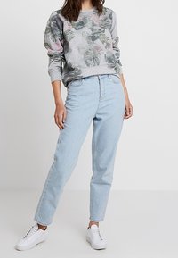 Sudadera gris claro con estampado de hoja verde, combinada con vaqueros de talle alto azul claro y zapatillas blancas. Corte casual y cómodo.