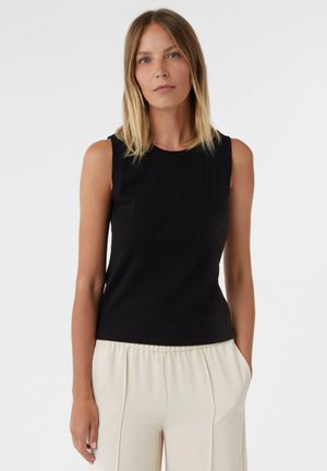 Schwarzes ärmelloses Top aus geripptem Material mit Rundhalsausschnitt, kombiniert mit hellen, plissierten Hosen, vor einem schlichten Hintergrund.
