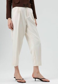 Witte hoge taillebroek met plooien, nauwsluitende pasvorm, lichtgewicht stof en cropped lengte. Gecombineerd met zwarte sandalen met bandjes.