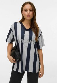 Grå og marineblå stripete kortermet V-hals skjorte med "MILANO 98" trykt på fronten. Brukt med svart clutch og mørke bukser.