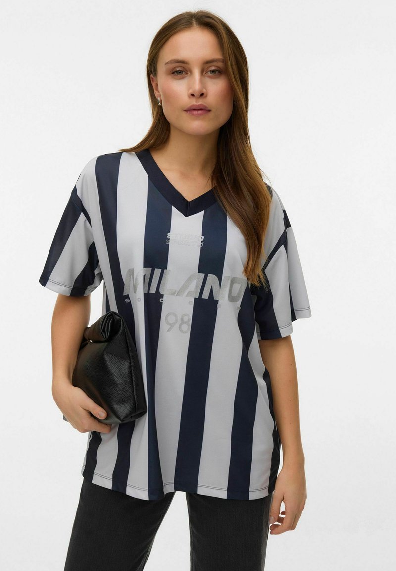 Grå og marineblå stripete kortermet V-hals skjorte med "MILANO 98" trykt på fronten. Brukt med svart clutch og mørke bukser.