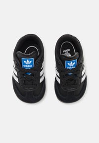 Svarta sportskor med vita ränder, med en ovandel i mocka och syntetmaterial, snörning och en blå adidas-logotyp på tungan.