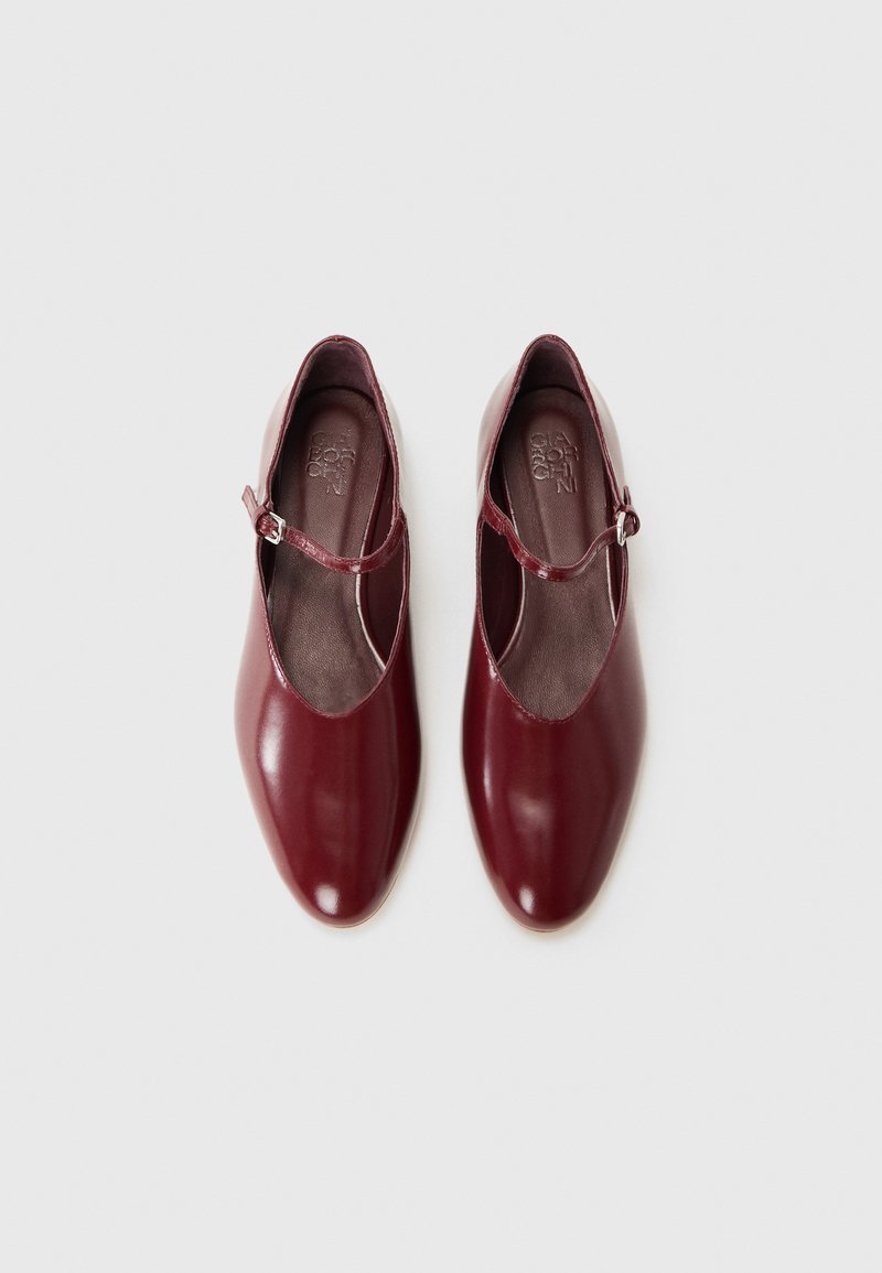 Burgundy leather shoes with a smooth finish, featuring a closed toe, ankle strap with buckle, and a minimalistic design.