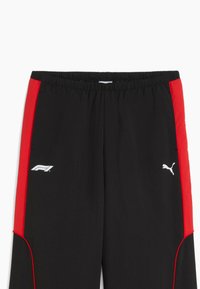Pantalons de sport noirs avec panneaux latéraux rouges, présentant des logos blancs : F1 à gauche et Puma à droite. Ceinture élastique pour un ajustement parfait.