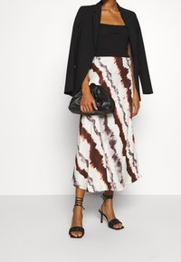 Svart kavaj över en ribbad svart croptop, kombinerad med en krämfärgad kjol med ett vågigt brunt mönster, och svarta strappy högklackade skor.