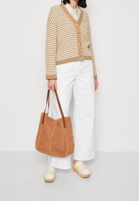 Gestreifter, brauner Cardigan mit Knöpfen, weiße Hosen mit weitem Bein, beiger Clog-Schuh und eine braune Ledertasche. Potenziell lässiger Alltagslook.