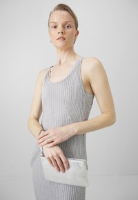 Hopeinen teksturoitu clutch-laukku, jossa on vetoketjukiinnitys. Yhdistetty vaaleanharmaaseen, ribatusta kankaan mekkoon, jossa on ohuet olkaimet. Neutraali, yksinkertainen muotoilu.