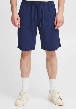 Mørkeblå bomullsshorts med elastisk midje og snor, med to frontlommer og en avslappet passform, brukt med hvite sokker og sko.