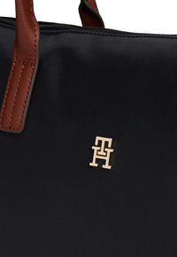 Črna platnena torba z rjavimi usnjenimi ročaji in zlatim kovinskim emblemom z vpletenim logotipom "TH".