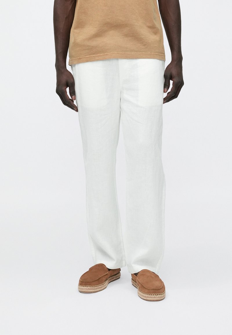 Hvide linnedbukser med en afslappet pasform og en glat tekstur. Parret med brune ruskindssko med flettede detaljer.