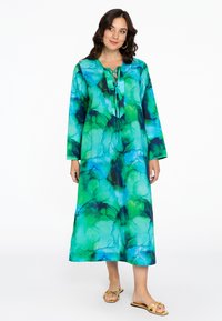 Lang jurkje in een blauw en groen abstract patroon met een V-hals, vetersluiting en lange mouwen, gemaakt van een lichtgewicht stof.