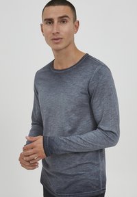 Langermet skjorte i blågrå farge laget av myk tekstil, med rund hals og kontrasterende sømmer på ermekantene. Diskret tekstur over hele skjorten.